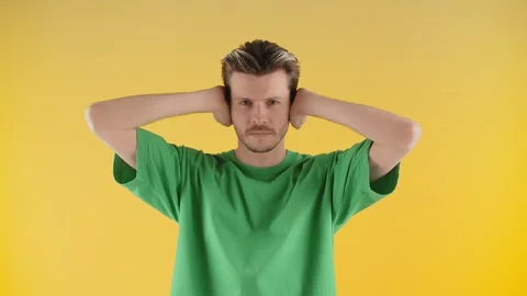 A person standing in front of a yellow background covers his mouth with his Stock Footage 240472142
