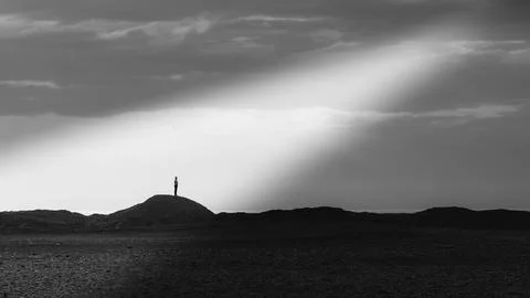 Person standing on hilltop under dramatic light beam in black and white Stock Photos
