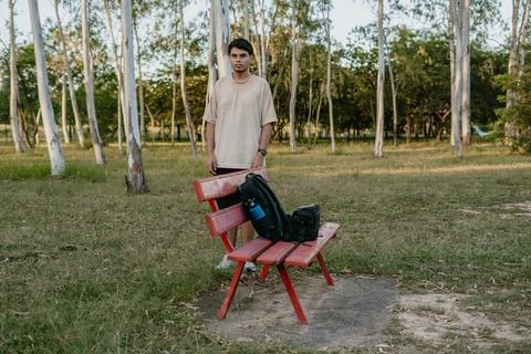 Person standing by a red bench with backpack, pause before moving on in a park Stock Photos
