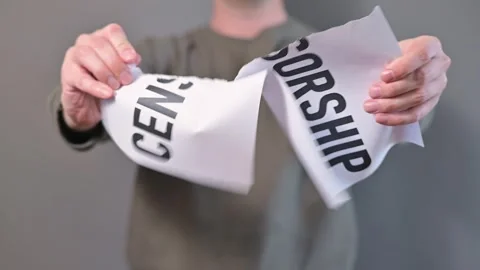 A person stands against a gray backdrop, holding a sign that reads Censorship. Stockbeeldmateriaal 338299953