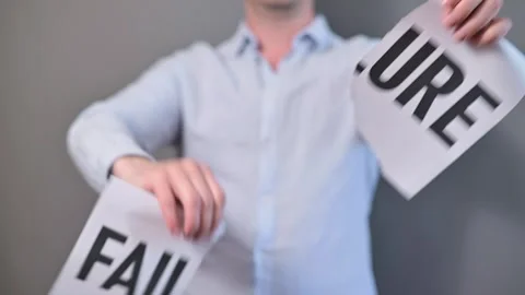 A person stands against a plain background, holding up signs that read failure. Видео 338299736