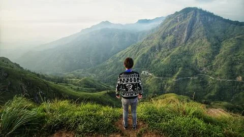 A person stands with his back to the camera against the backdrop of mountains Stock Photos