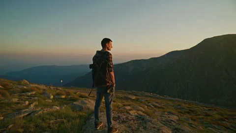Person stands on a rock looking at mountain landscape during sunset in a natural Stock Footage 345634115