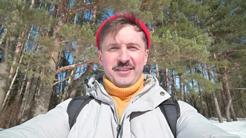 A person stands in a snowy forest while smiling and waving. The individual is 스톡 동영상 337101569
