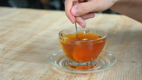 Person steeping tea with teabag in clear glass cup on wooden table Stock Footage 274181376