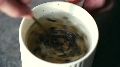 Person stirring loose leaf tea infusion in white mug Stock Footage 323720270