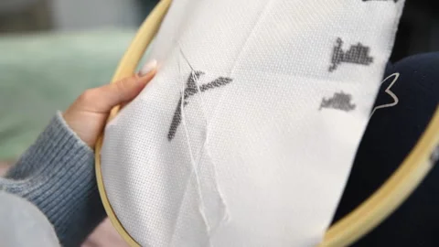 Person stitching black thread design on white fabric with embroidery hoop i.. Stock Footage 334955115