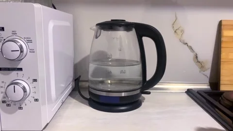 Person switching on electric kettle, close-up view beside a microwave Stock Footage 345361704