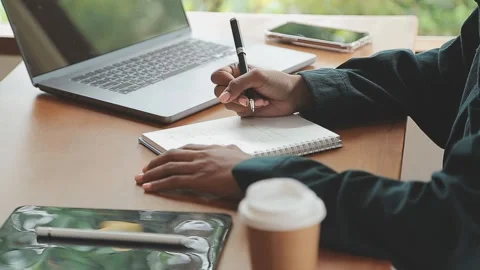 Person takes notes with pen at desk with laptop and other devices Stock Footage 325308868