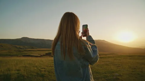 A person takes a picture with a smartphone while standing in a green field Stock Footage 345639940