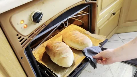 Person taking freshly baked bread out of the oven in a cozy home kitchen Stock Footage 332076386