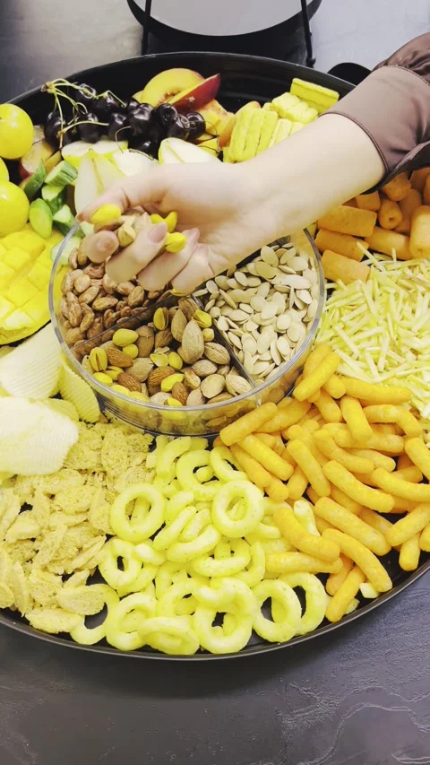 Person taking nuts and seeds from a partitioned bowl on a tray Stock Footage 345146333