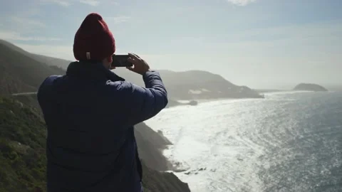 Person taking pictures of the ocean with their phone on the edge of a cliff. Stock Footage