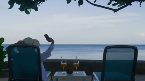 Person taking selfie at beachfront table with tropical drinks Stock Footage 346367273
