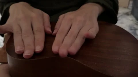 Person tapping fingers rhythmically on back of ukulele body close up at home, Stock Footage 337105436