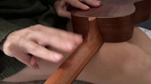Person tapping fingers rhythmically on ukulele neck close up at home, producing 库存影片 337105516