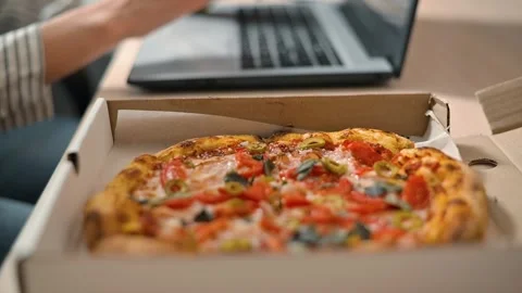 A person is tapping on a laptop while sitting at a table with a pizza in front. Stock Footage 339005465