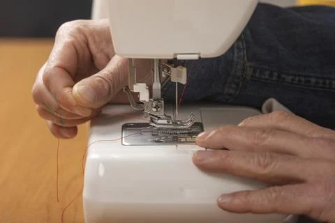 Person threading red spool into sewing machine needle Stock Photos