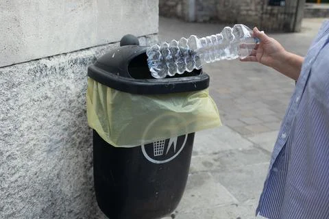 Person throwing empty plastic water bottle into public garbage bin outdoors Stock Photos