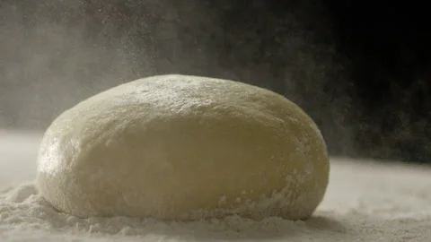Person throwing flour over ball of dough on counter black background Stock Footage 274689265