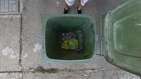 Person throwing plastic garbage bag into open green trash bin from above Stock Footage 346070201