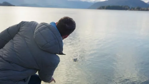 Person throwing rocks or pebbles to lake waters skipping stones in Wanaka Lake Stock Footage 289416672