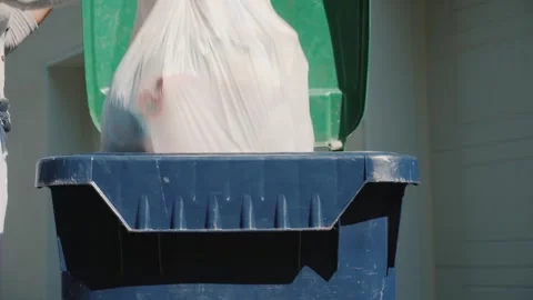 Person throwing waste into blue plastic garbage bin outside residence. Stock Footage 334586823