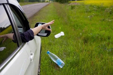 A person throws garbage from the car window to the side of the road Stock Photos