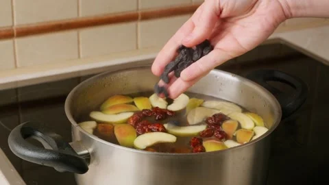 A person throws a handful of dark raisin into a saucepan of cooking compote Stock Footage 308157759