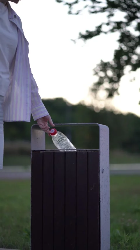 Person throws plastic bottle into outdoor park trash bin at dusk Video stock 341895066