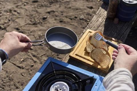 Person toasts bread outdoors, using a frying pan on a gas portable stove. Foto stock