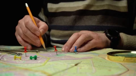 Person topographer marking locations on a map with colored pins and a pencil, Stock Footage 332649395
