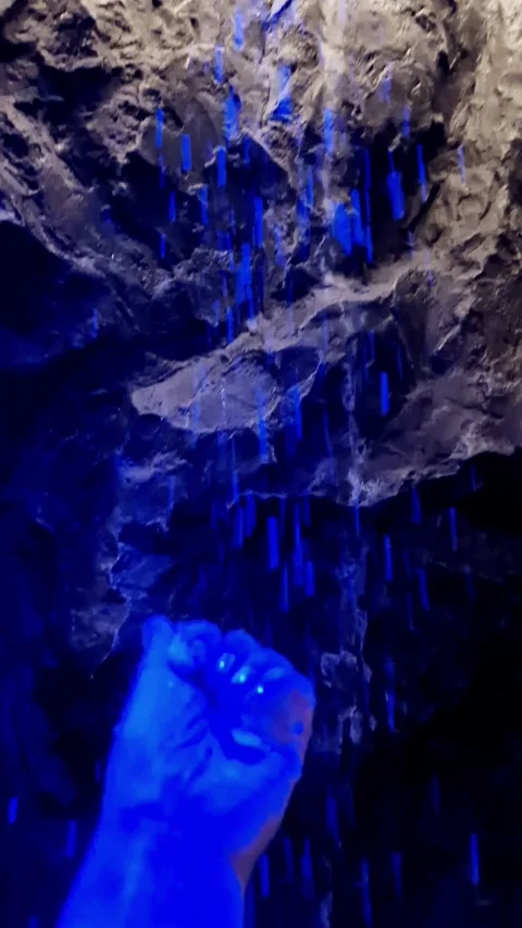 Person Touching Falling Blue Water Streams in Dark Stone Interior Stock Footage 338992935