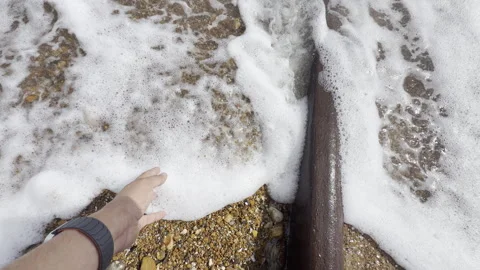 Person touching ocean foam by pipe panning Stock Footage 338131897