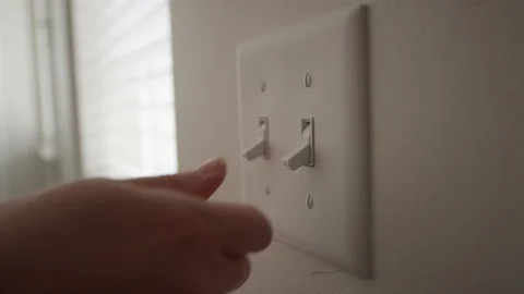A person turn a light switch on during the day inside a home Video stock 128918830