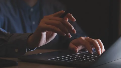 Person typing on computer and holding phone in dark room at night Stock Footage 325351263