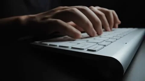 Person typing on a computer keyboard in a dark setting 스톡 사진