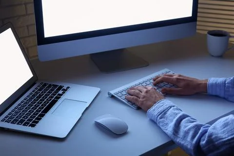 Person typing on a computer keyboard at night with bright screens, remote wor Stock Photos