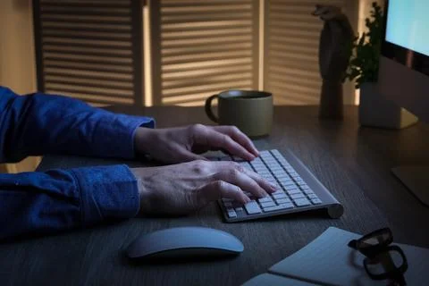 Person typing on computer keyboard at night, remote work and online communica Stock Photos
