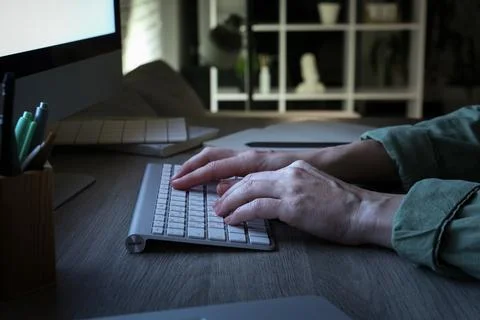 Person typing on computer keyboard at night, remote work and online communica Stock Photos