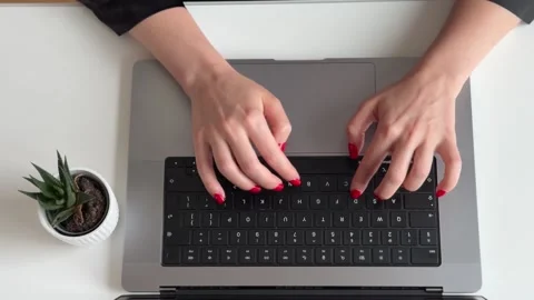 A person typing on a laptop with red nails and a plant nearby. 스톡 동영상 340526546