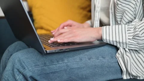 A person is typing on a laptop while seated comfortably on a couch in a living Stock Footage 338446206