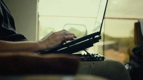 Person typing on laptop while sitting on sofa near window Stock Footage 324859329