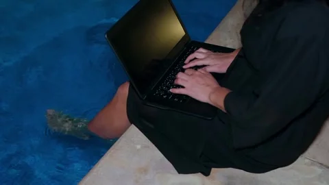 Person typing on laptop while sitting poolside at night Video stock 341423884
