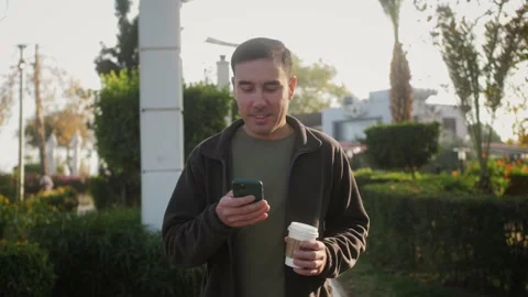 Person typing on smartphone and drinking delicious coffee during stroll at park. Stock Footage 239615015