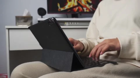 Person typing on tablet on her lap while sitting on a chair Stock Footage 276932726