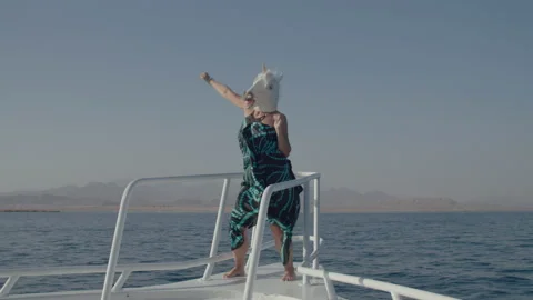 Person in unicorn head mask dancing on boat nose. Funny dancings of unicorn mask Stock Footage 162735563