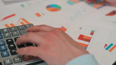 A person uses a calculator while examining various sheets of paper and charts Stock Footage 338188284