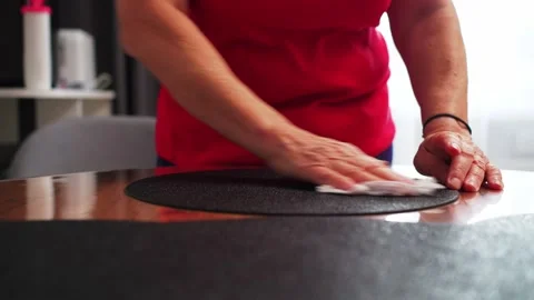 A person uses a cloth to wipe a round black mat placed on a wooden table. Stock Footage 330073145