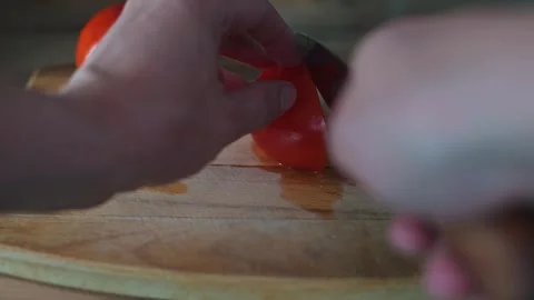 A person uses a knife to slice fresh tomatoes on a wooden cutting board in a Stock Footage 339096214